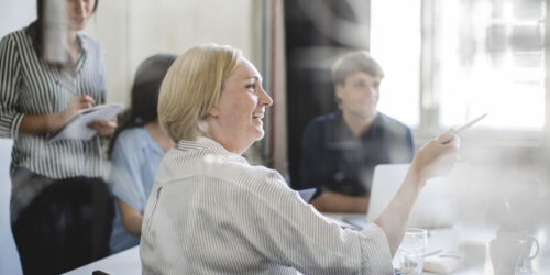 Smiling businesswoman pointing while sitting with colleagues in board room during meeting